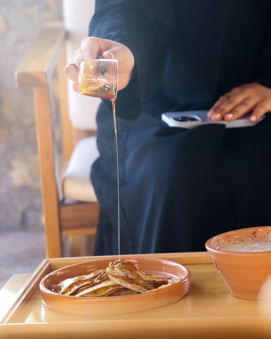 يدٌ تسكب العسل على قروص شَمْل في صحن فخّاري — لحظة إفطار عُماني