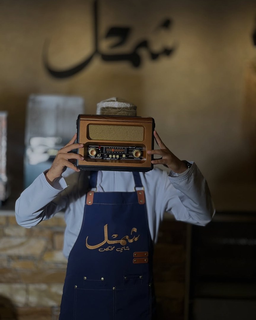 باريستا شَمْل برداء العمل يحمل راديو كلاسيكياً أمام جدارية اسم شَمْل